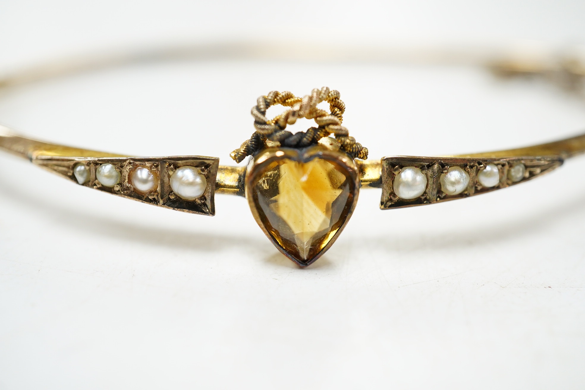 A Victorian yellow metal, citrine and seed pearl set hinged bangle, with heart shaped citrine, interior diameter 62mm, gross weight 4.6 grams, with fitted leather box. Condition - poor